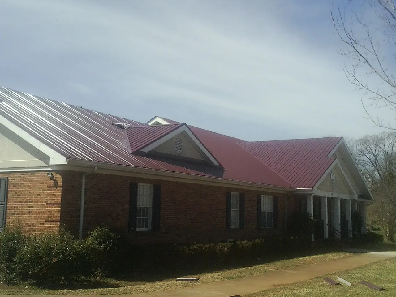 Red metal roof with gabled entries on a long brick building, from a Hail Damage Roof Repair job in Woodbine